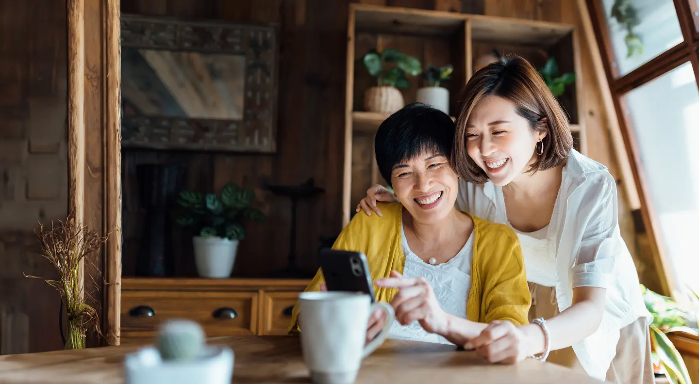 An older and younger woman look at a phone together while smiling